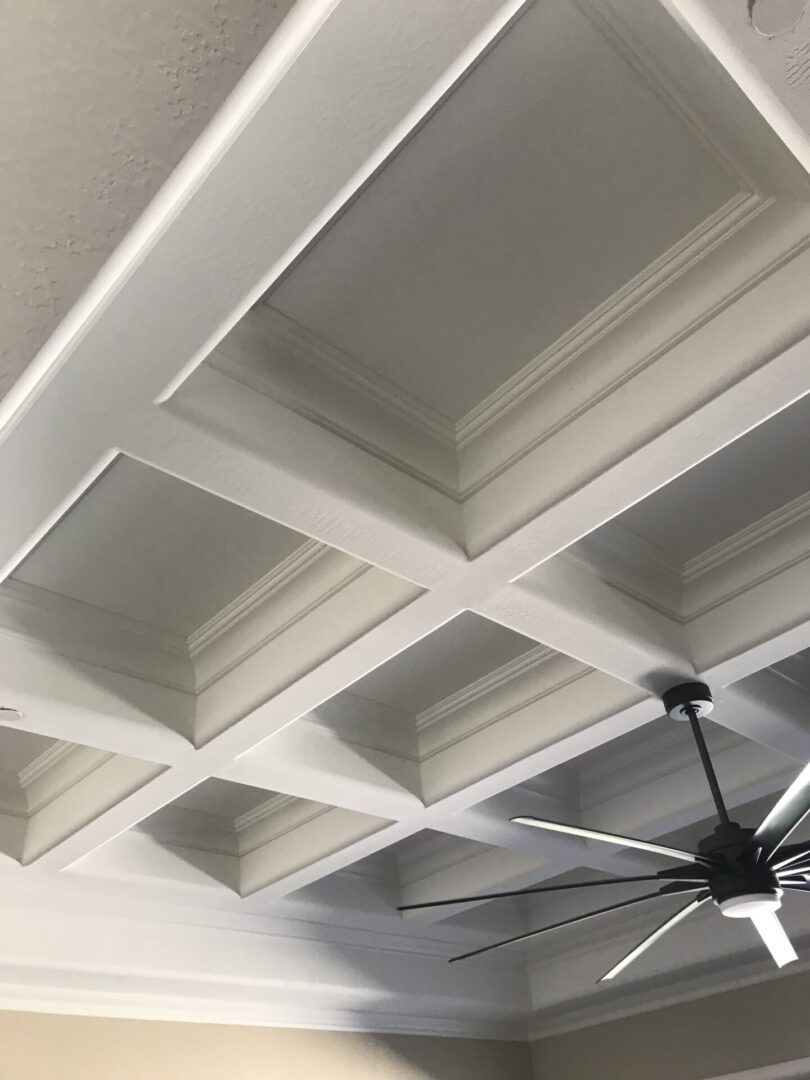 A ceiling with many white ceilings and one fan