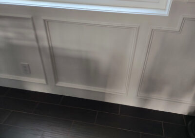 White baseboard below decorative wall moulding and a window above dark tile flooring.