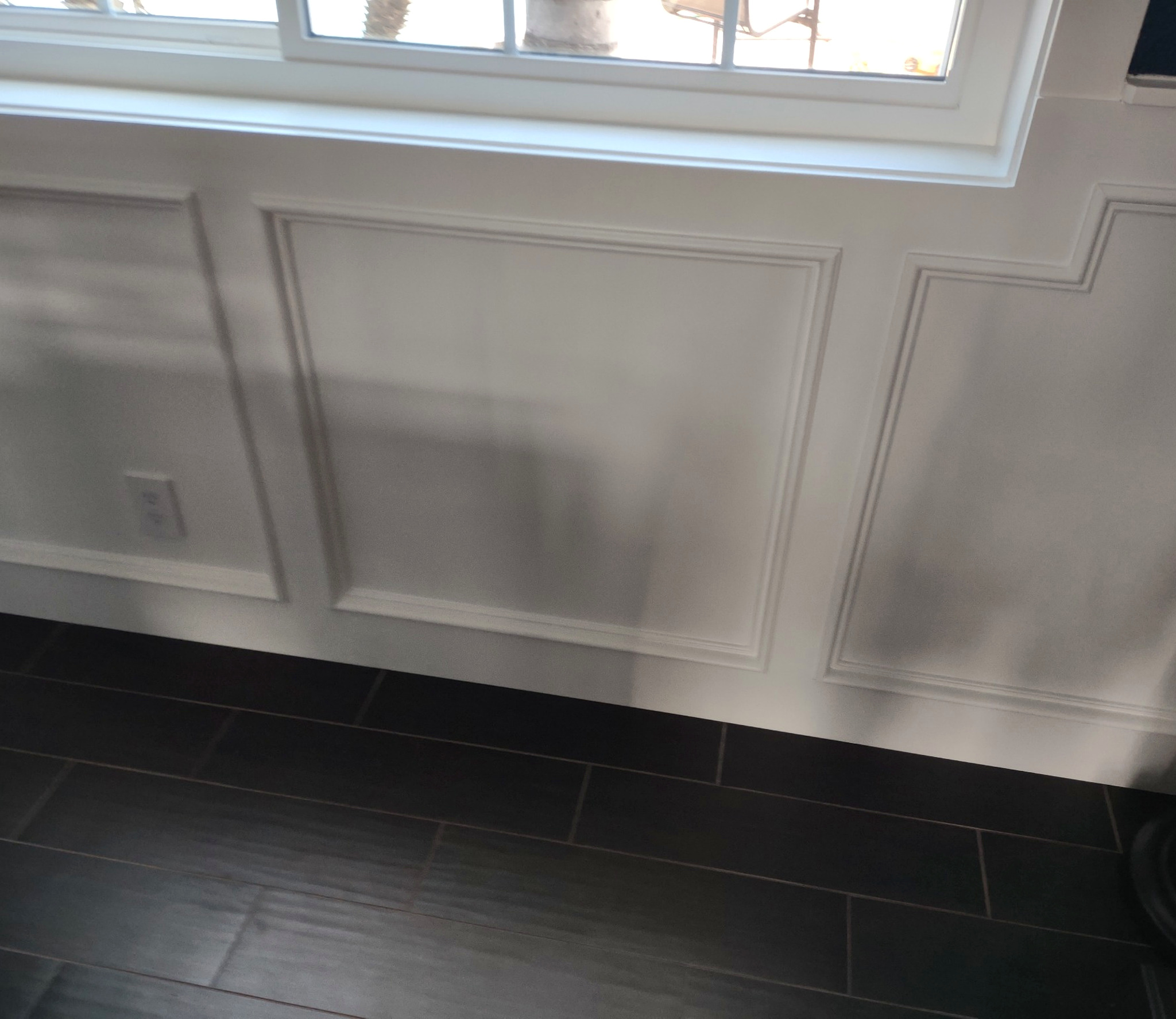 White baseboard below decorative wall moulding and a window above dark tile flooring.