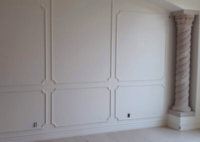 White baseboard moulding extending beneath an ornate wall design beside decorative columns.