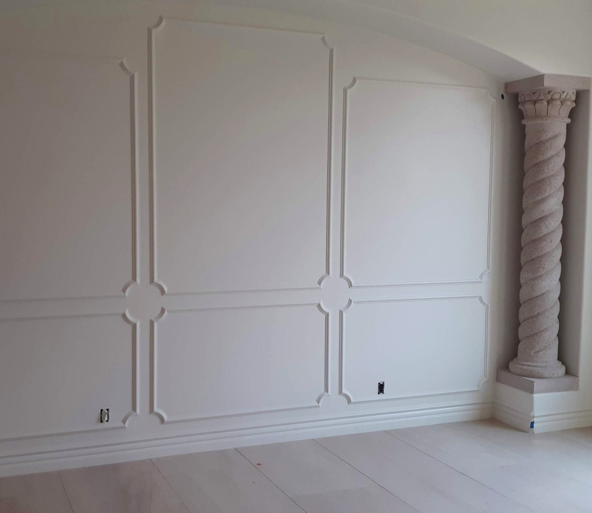 White baseboard moulding extending beneath an ornate wall design beside decorative columns.