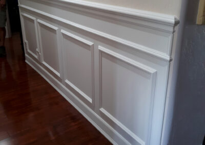 Layered white baseboard and decorative wainscoting beside dark hardwood flooring.