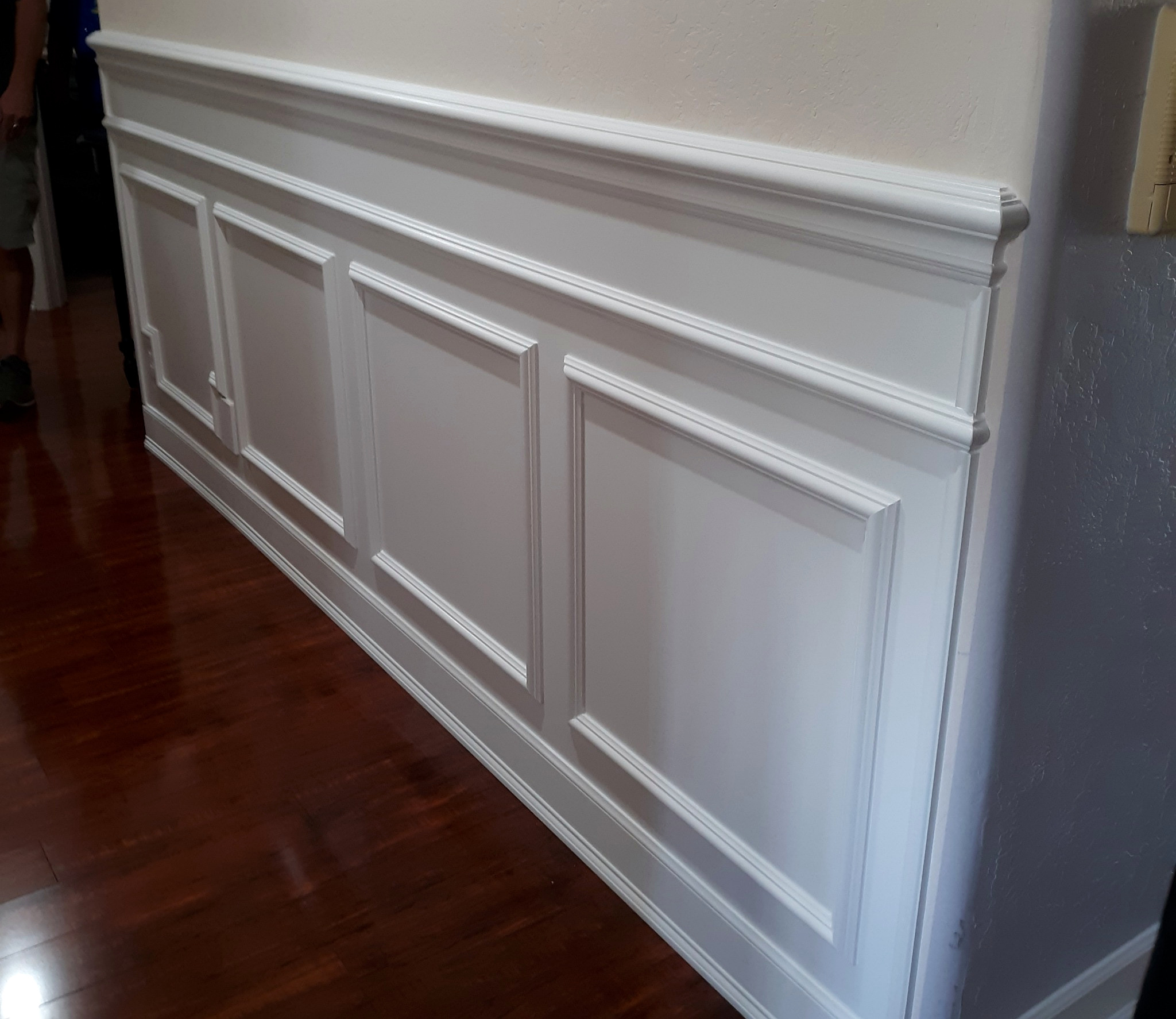 Layered white baseboard and decorative wainscoting beside dark hardwood flooring.