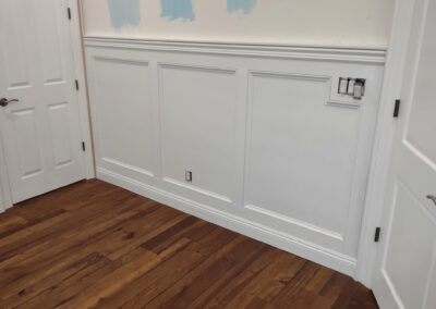 White baseboards along decorative wall panels above warm hardwood flooring.
