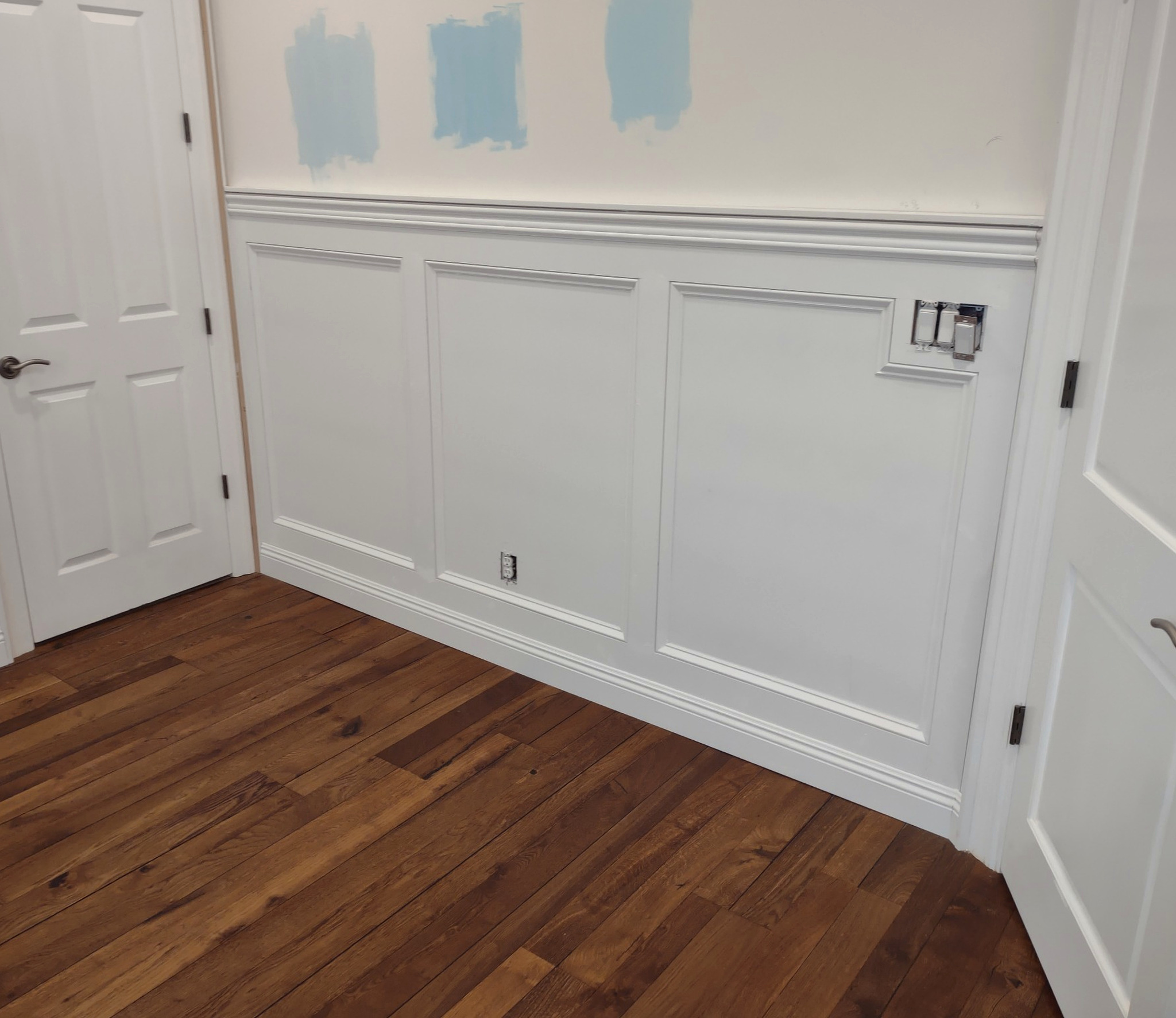 White baseboards along decorative wall panels above warm hardwood flooring.