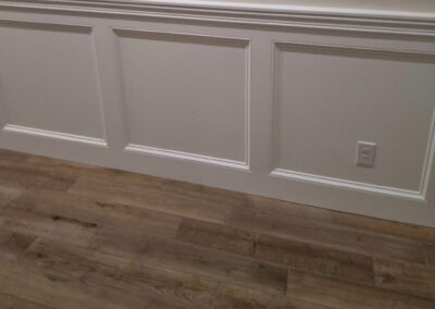 White baseboard trim beneath decorative wall panels beside wood flooring.