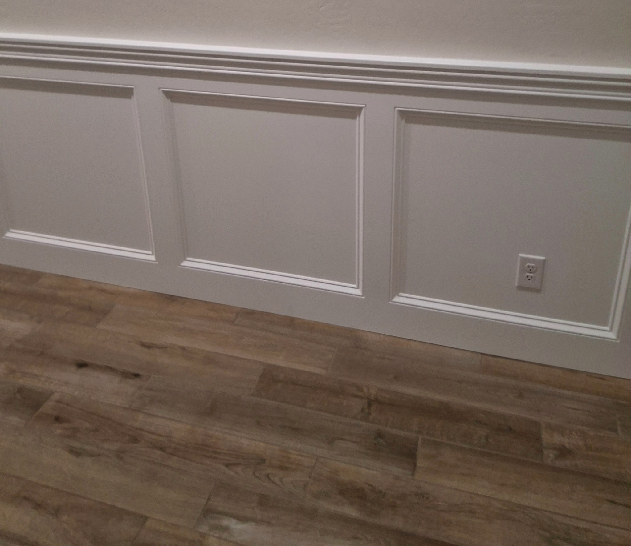 White baseboard trim beneath decorative wall panels beside wood flooring.