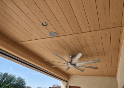 Painted tongue and groove ceiling on a covered patio with decorative beams, recessed lights, and a ceiling fan.