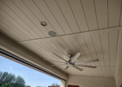Painted tongue and groove ceiling on a covered patio with decorative beams, recessed lights, and a ceiling fan.